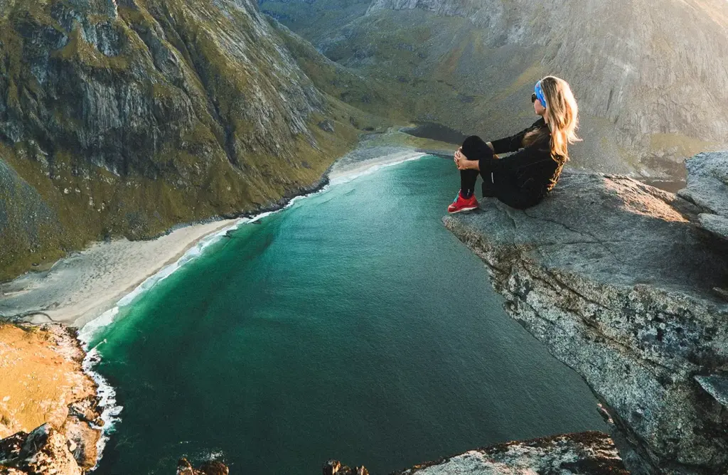 Turkuaz renkli kıyı sularına ve ıssız bir Norveç sahiline bakan bir uçurumun üzerinde oturan gezgin