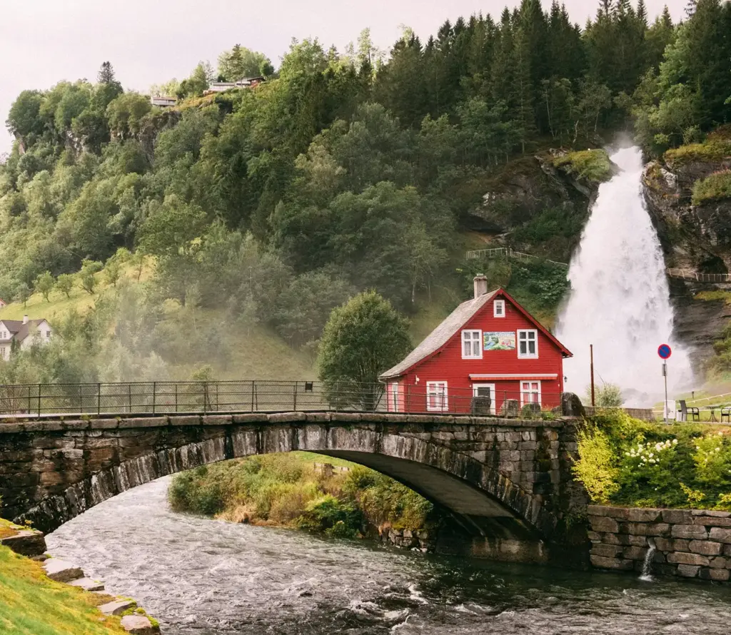 Norveç kırsalındaki bir köyde, şelale ve taş köprünün yakınında bulunan geleneksel kırmızı ev